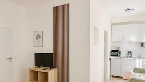 Una habitación de hotel moderna con cama, televisor, escritorio pequeño y kitchenette.