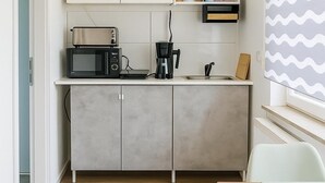 Una kitchenette compacta con microondas, cafetera y un estante pequeño con utensilios de cocina.