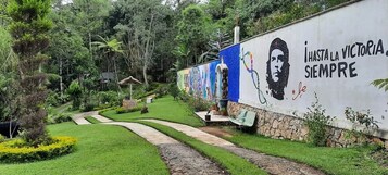 Un sendero en un jardín que conduce a un edificio con un mural y el texto "I HASTA LA VICTORIA SIEMPRE".