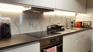 Eine moderne Küche mit weißen Schränken, einer schwarzen Arbeitsplatte, einem eingebauten Backofen, einer Edelstahl-Dunstabzugshaube, einem Spülbecken mit Armatur und einer Kaffeemaschine.