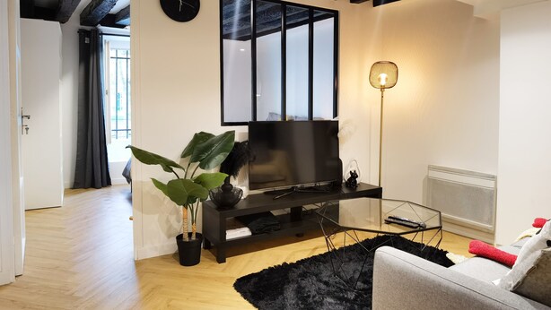 Ein modernes Wohnzimmer mit einem Flachbildfernseher, einer schwarzen Unterhaltungsecke, einem Glastisch und einem grauen Sofa, sowie einem schwarzen Teppich.