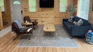 A cozy cabin interior with wooden walls, a flat-screen TV, a sofa, a coffee table, and a chair.