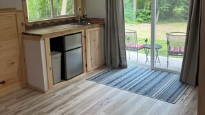 A compact kitchen with a built-in refrigerator, a sink, and a window overlooking a forest.