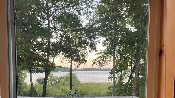 A deck with a table and chairs, overlooking a lake and trees.