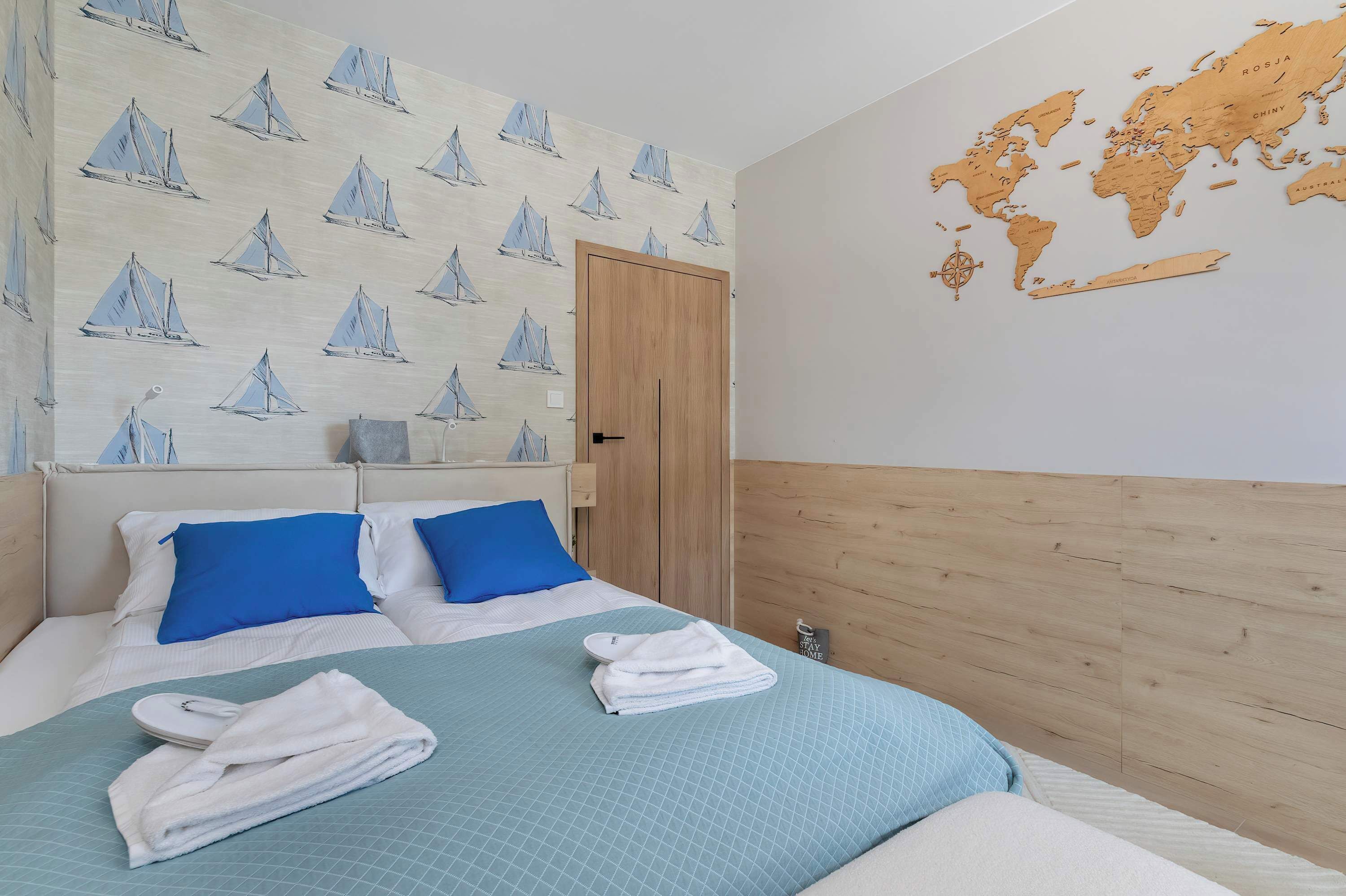 A hotel room with a bed, blue pillows, a world map on the wall, and a wooden headboard.