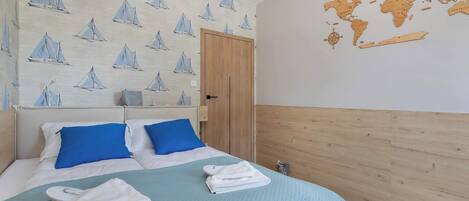 A hotel room with a bed, blue pillows, a world map on the wall, and a wooden headboard.