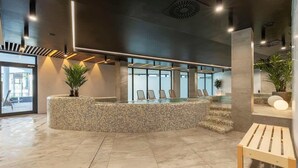 A modern lobby with a circular seating area, a reception desk, and a staircase leading to upper floors.
