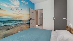 A bedroom with a large wall mural of a beach scene, a bed with a blue bedspread, and a bedside table with a lamp.