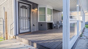 Un porche abrité avec une terrasse en bois, une entrée fermée par un portail et un espace détente avec des chaises.