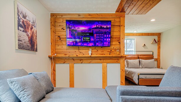 Une pièce confortable avec un lit, un canapé et un téléviseur fixé au mur, qui est en bois.