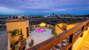 A modern resort with a pool, outdoor seating, and a view of the beach at dusk.