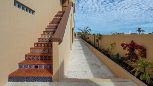 A staircase with colorful tiles leading to a door, a pathway with plants, and a clear sky.
