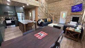 Un amplio salón con una gran mesa de comedor de madera oscura, una cocina con electrodomésticos modernos, una chimenea de piedra y una zona de estar acogedora con un sofá y sillones.