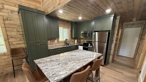 Una cocina moderna con gabinetes verdes, encimera de mármol y electrodomésticos de acero inoxidable.
