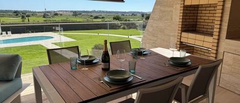 Un espacio de comedor al aire libre con vistas a una piscina y un paisaje con césped.