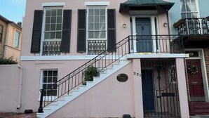 A multi-story building with a pink facade, black shutters, and a green awning.