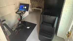 A compact gym area with a stationary bike, a treadmill, and a black exercise machine.