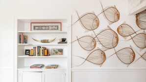 Una estantería blanca con libros y objetos decorativos, un armario blanco debajo y una pared con arte abstracto de alambre en forma de peces.