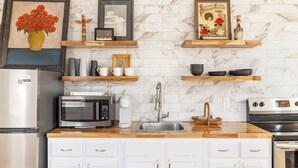 Una cocina con armarios blancos, un microondas, un fregadero y una estufa. Hay objetos decorativos en los estantes sobre la encimera.