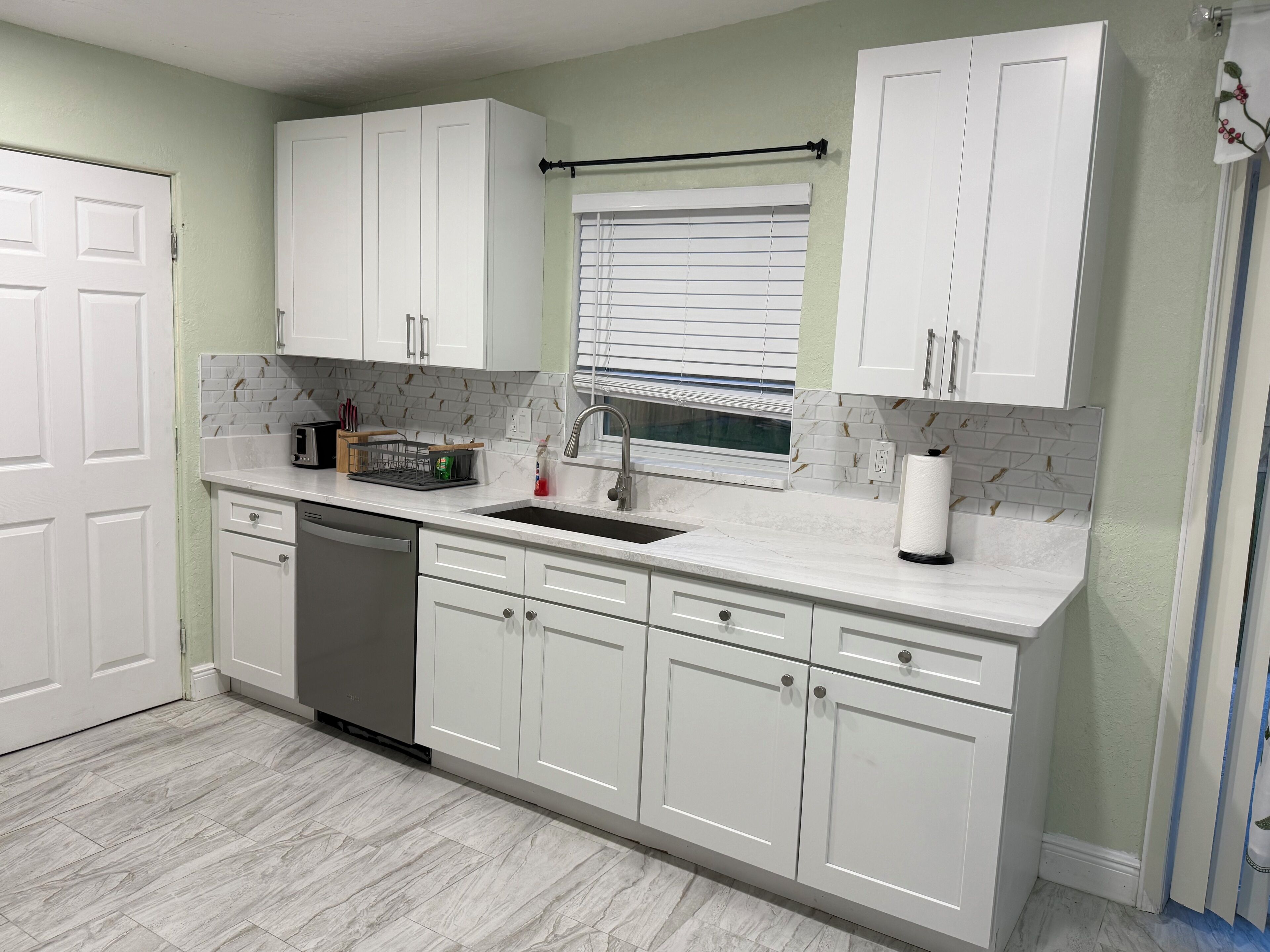A kitchen with white cabinets, a dishwasher, a sink, and a window with blinds.