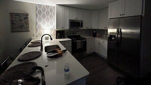 A compact kitchen with white cabinets, a stainless steel refrigerator, a microwave, and a stove.