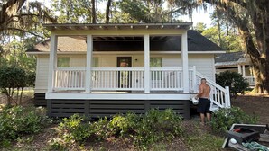 A two-story house with a porch, surrounded by greenery and trees.