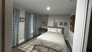 A bedroom with a bed, curtains, a bedside table, a wall-mounted artwork, and a window with blinds.