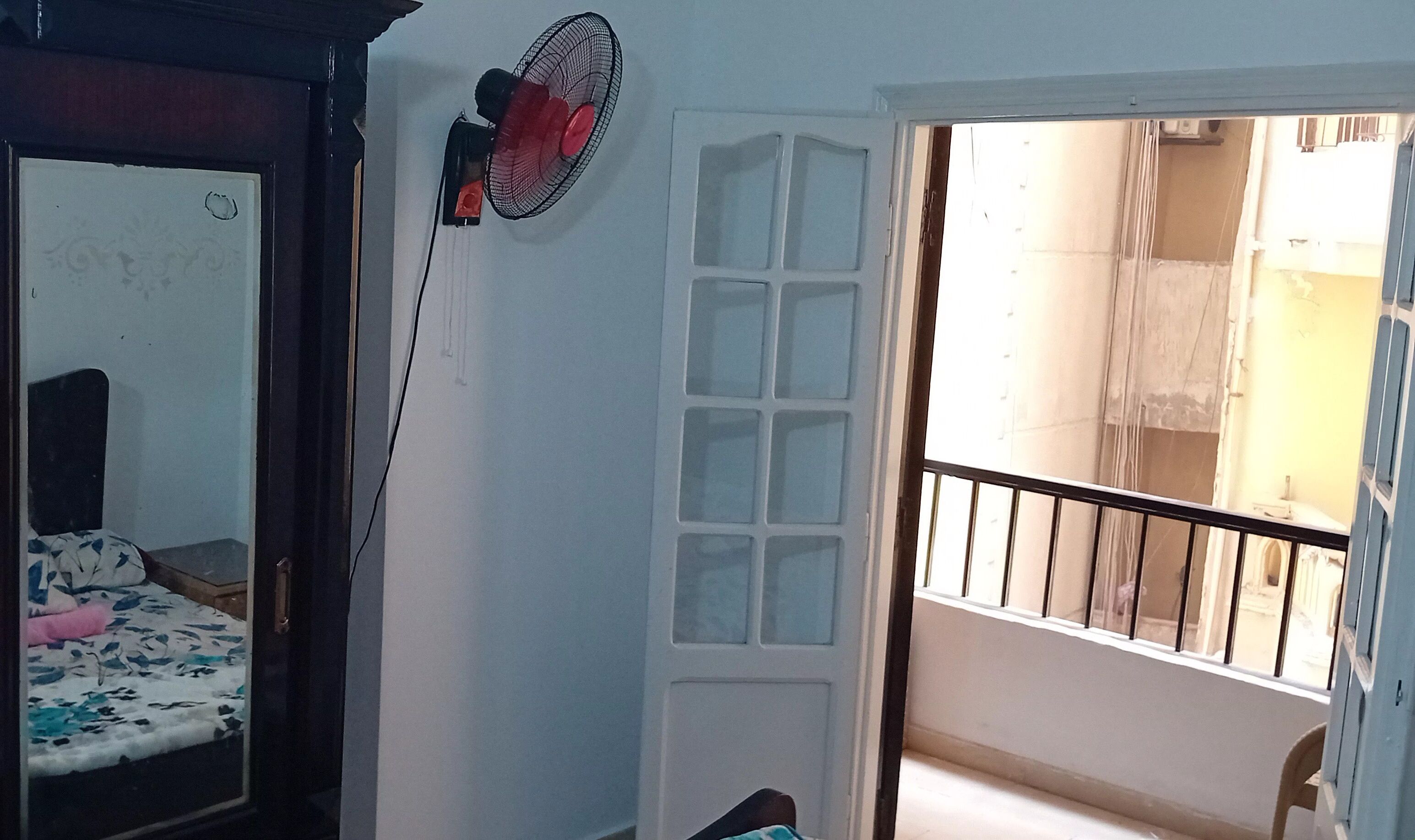Een kamer met een bed, een ventilator aan de muur en een deur naar een buitenruimte.