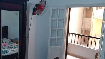 Een kamer met een bed, een ventilator aan de muur en een deur naar een buitenruimte.