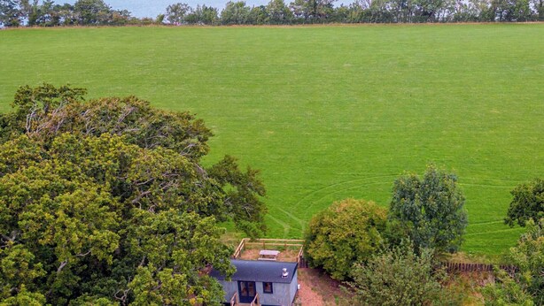 An aerial view of a small house with a fenced yard and a large open field in the background. - Cwt Clyd-Shepherd’s Hut (Bangor)