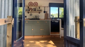 A compact kitchen with a central island, wooden cabinets, and a window providing natural light. - Cwt Clyd-Shepherd’s Hut (Bangor)