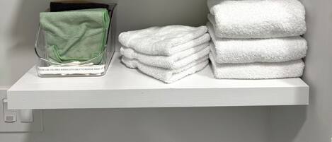 A bathroom with white towels stacked on shelves, a green towel dispenser, and a small potted plant.