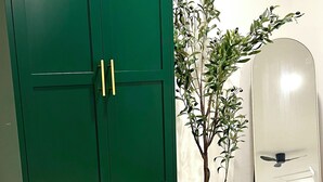 Une armoire verte avec trois tiroirs et deux portes, une plante en pot et un miroir avec un ventilateur de plafond.