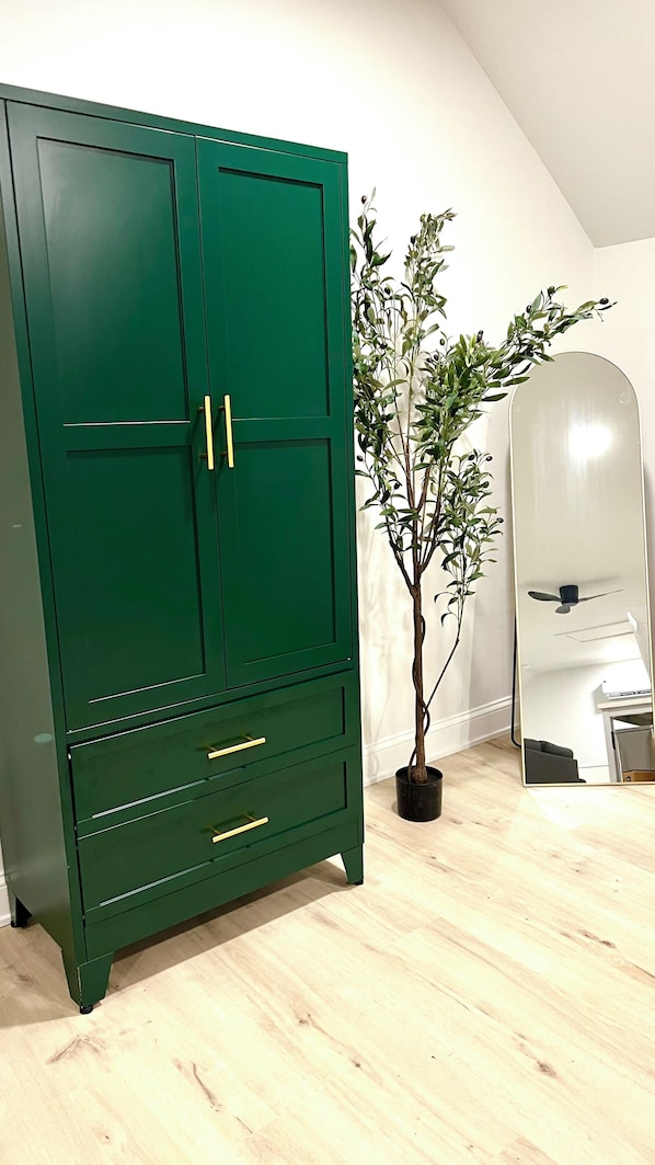 Un armario verde con tres cajones y dos puertas, una planta en maceta y un espejo con ventilador de techo.