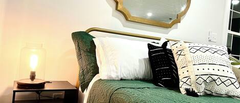 A neatly made bed with green bedding, a bedside lamp, and a mirror on the wall.