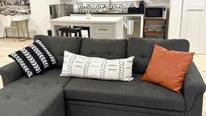 A modern living room with a grey sectional sofa, a coffee table, and a kitchen in the background.