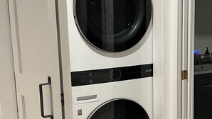 Une machine à laver fixée au mur, dotée de deux grands tambours cylindriques, d’un panneau de commande et d’un petit compartiment de rangement.