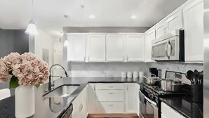 Una cocina moderna con armarios blancos, encimera negra, electrodomésticos de acero inoxidable y un jarrón con flores.
