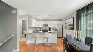 Una cocina moderna con armarios blancos, una isla central con taburetes altos y una zona de comedor con mesa y sillas.
