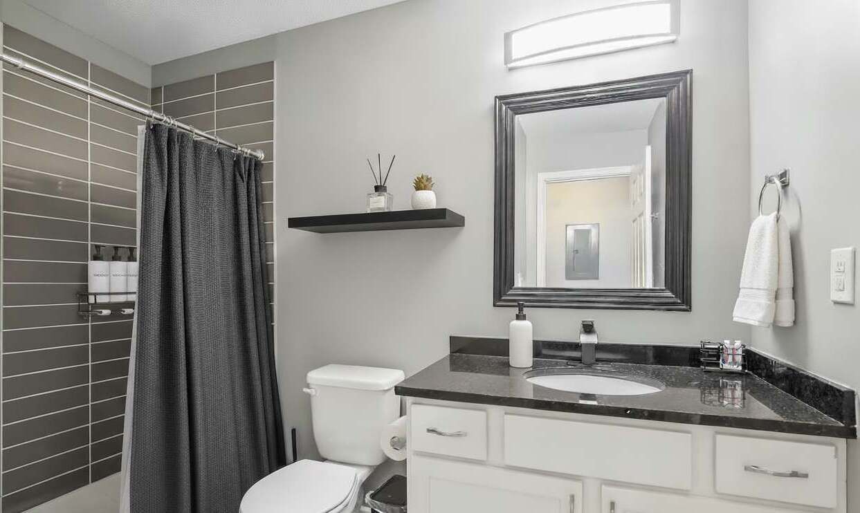 A modern bathroom with a shower curtain, toilet, sink, and mirror.
