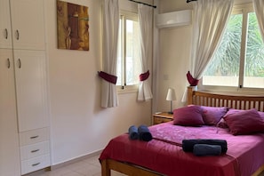 Un dormitorio con cama, mesita de noche, ventana con cortinas y aire acondicionado de pared.
