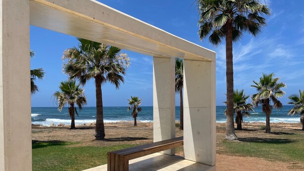 A beach view with palm trees and a bench under a white structure. - Holiday Home Paphos - Near Amenities - Poolside (Paphos)
