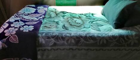 A bed with a floral bedspread, a green pillow, and a headboard with a light fixture.