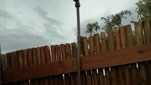 Una valla de madera con una tubería metálica y un objeto metálico adherido.