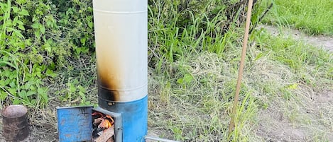 A cylindrical water tank with a blue base, connected to a metal pipe system, set in a natural environment with dense greenery in the background.
