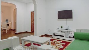 Ein Wohnzimmer mit einem an der Wand montierten Flachbildfernseher, einer weißen Unterhaltungsanlage, einem grünen Sofa und einem roten Teppich mit Blumenmuster.