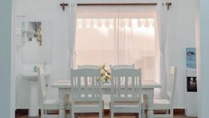 Ein Essbereich mit weißem Tisch und Stühlen, einem Deckenventilator und einem Fenster mit Vorhängen.