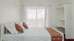 Ein Schlafzimmer mit einem Bett, einem Fenster mit Vorhängen, einem Deckenventilator und einem weißen Kleiderschrank.
