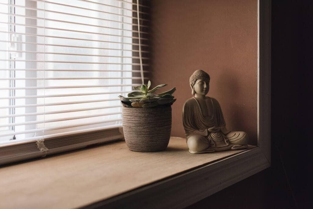 Una ventana con una planta en maceta y una estatua de Buda en el alféizar.