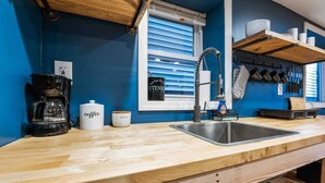 Una cocina con encimera de madera, un lavamanos de acero inoxidable, una cafetera y una ventana con persianas.